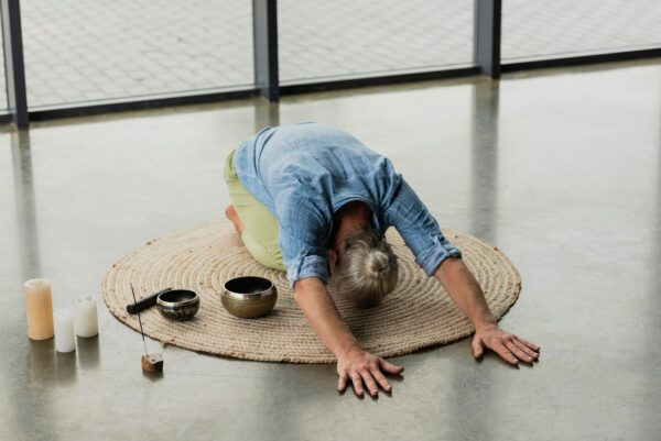 grey haired man stretching back near Tibetan singing bowls and incense stick in yoga studio