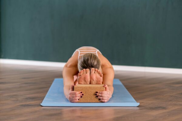 Flexible woman stretching back holding on to yoga block while sitting on blue mat